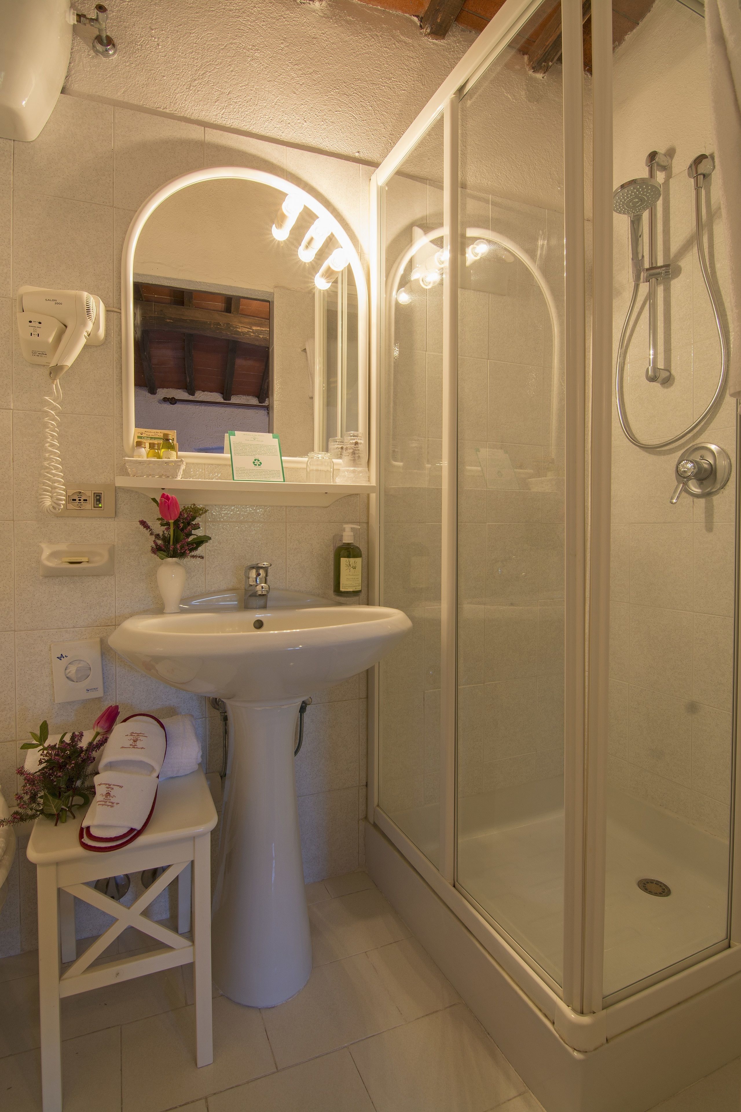A bathroom with a glass-enclosed shower, a pedestal sink, and a vanity with a mirror.