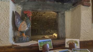 Un interior rústico con una chimenea de ladrillo, un gallo decorativo y varias fotografías enmarcadas sobre una mesa de madera.