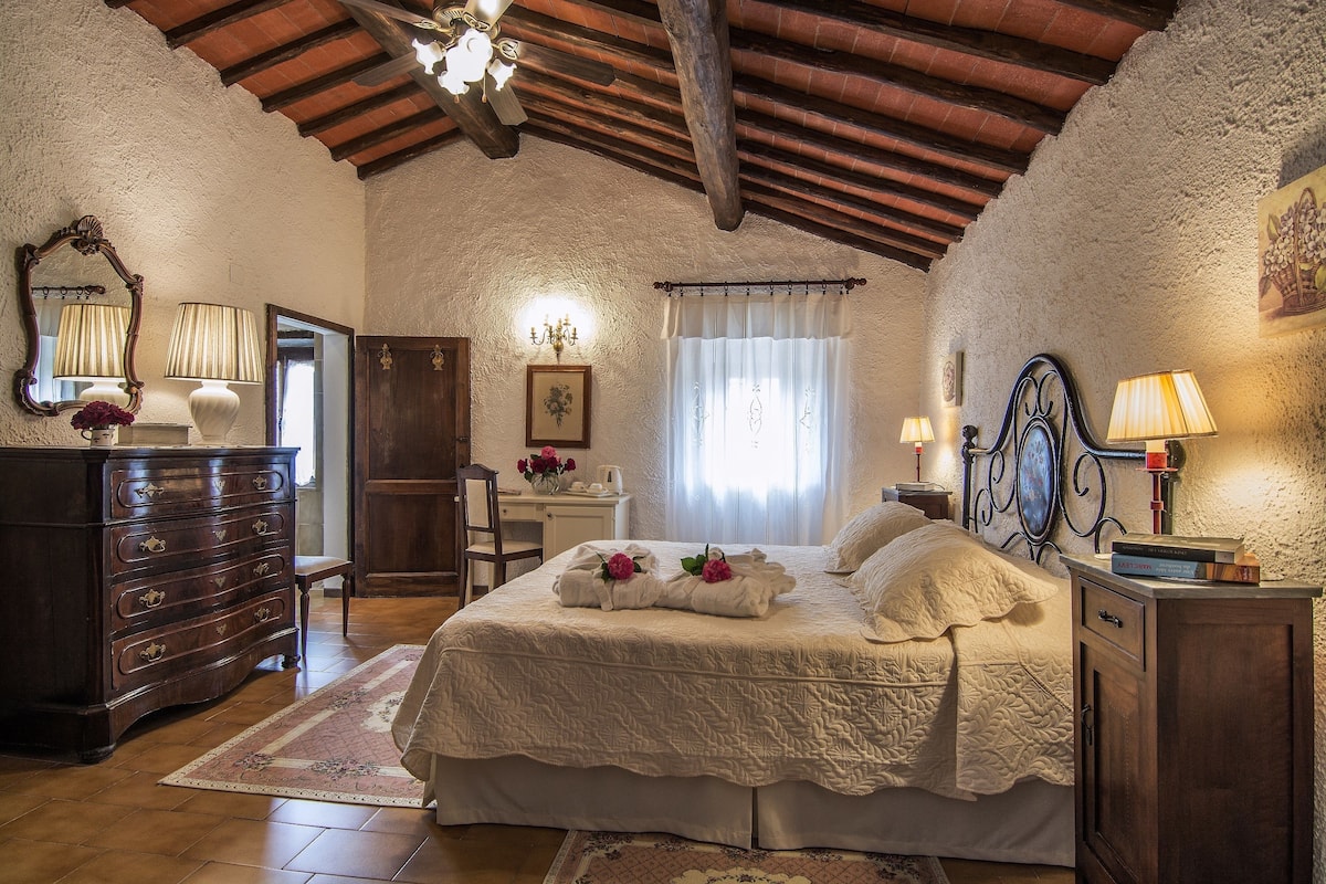 A bedroom with a large bed, wooden furniture, a chandelier, and a rustic ceiling.