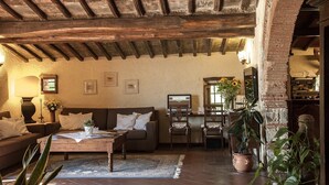 A rustic living room with exposed wooden beams, a sofa, a coffee table, and a dining area with chairs. - Hotel Colle Etrusco Salivolpi (Castellina in Chianti)