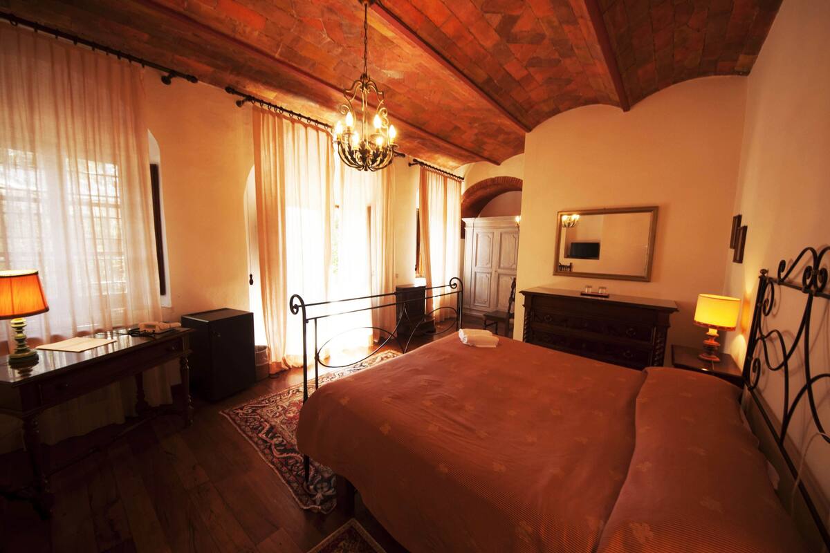 Un dormitorio con una cama grande, un escritorio de madera, un aparador, un espejo y una araña.
