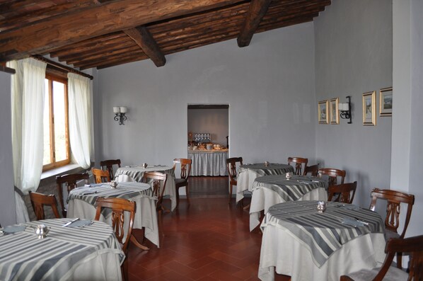 A dining area with multiple tables, wooden chairs, and a kitchen in the background. - Villa Casalecchi Country Hotel (Castellina in Chianti)
