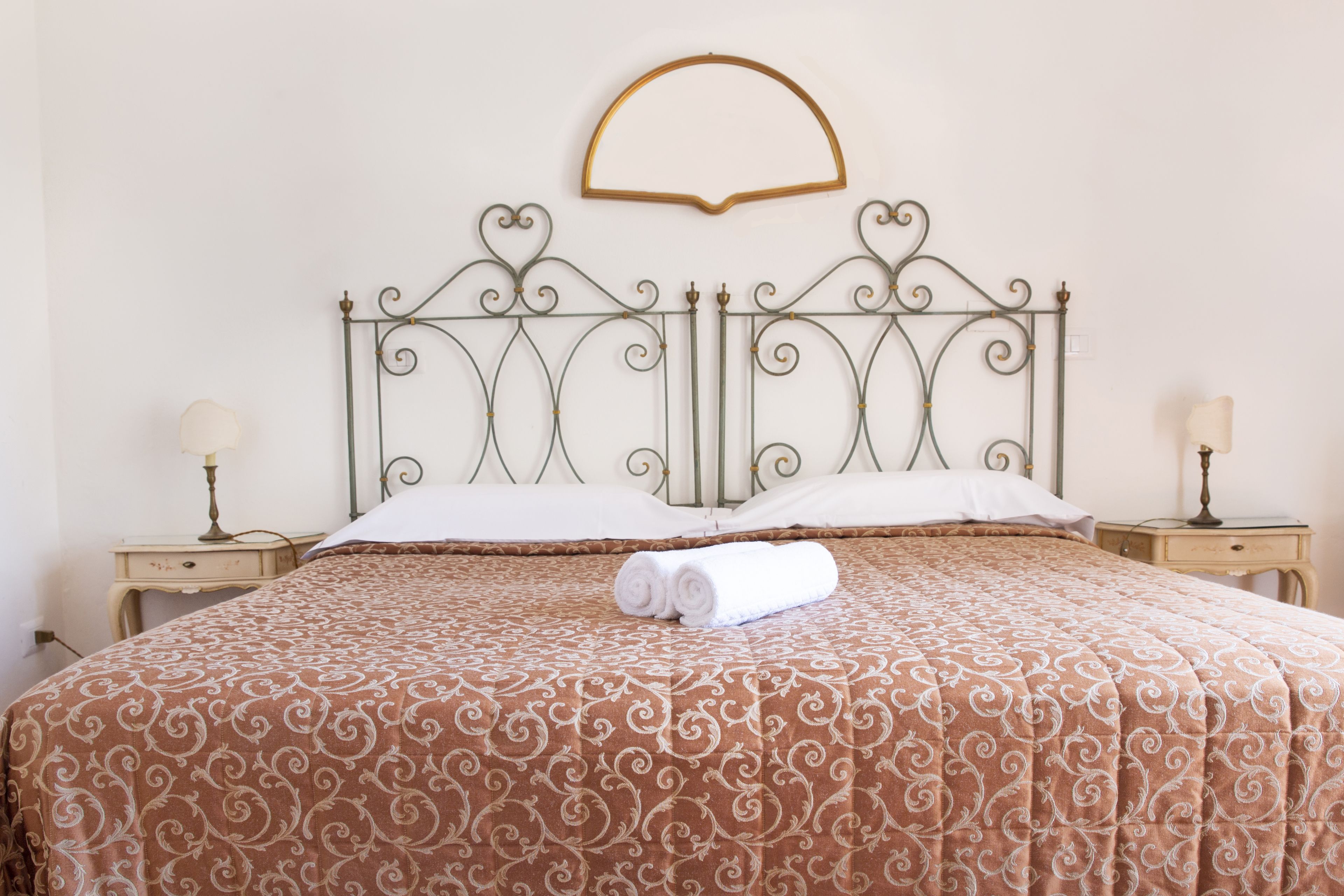 A neatly made bed with a patterned bedspread, two bedside tables with lamps, and a decorative wall hanging above the bed.