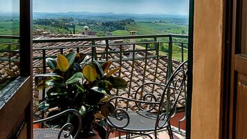 Un balcon offrant une vue sur un paysage verdoyant et des collines lointaines. On y trouve deux chaises en métal et une plante en pot.