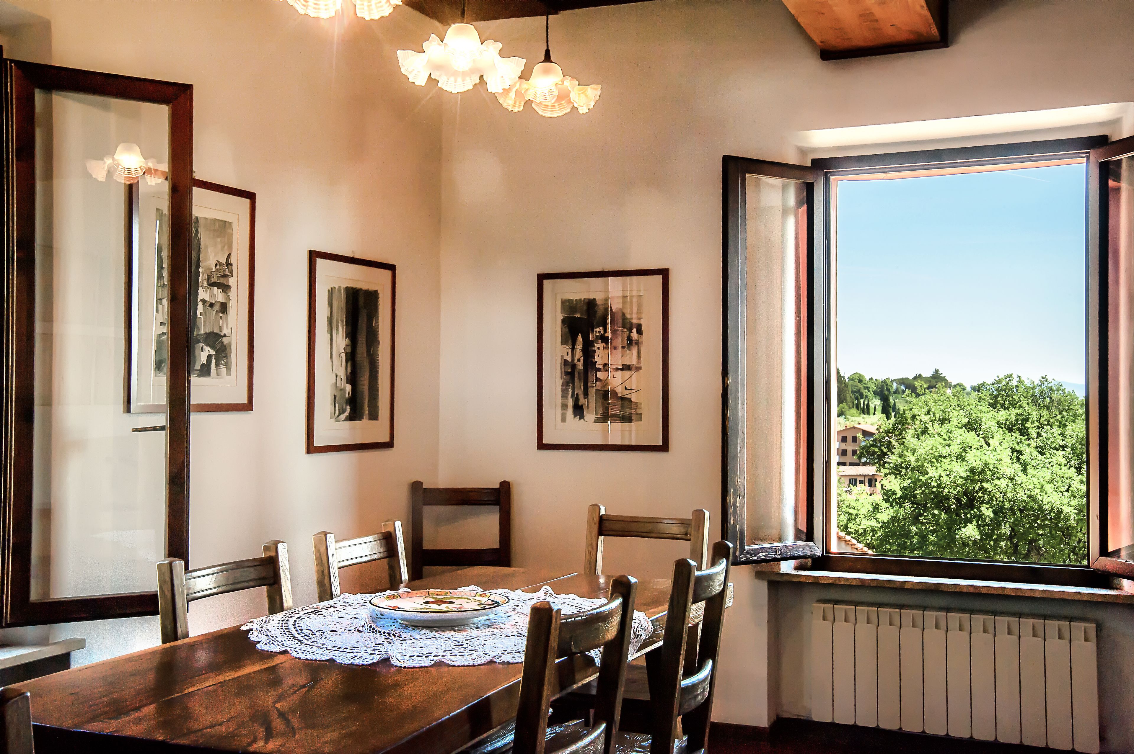 Un comedor con mesa de madera, sillas, cuadros en la pared y ventana con vistas a árboles.