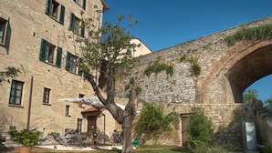 A stone building with a large archway, a tree in the foreground, and outdoor seating. - Arnolfo B&B (Colle di Val d'Elsa)
