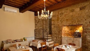 A dining area with stone walls, wooden beams, and a chandelier. Tables are set with white tablecloths and tea sets. - Arnolfo B&B (Colle di Val d'Elsa)