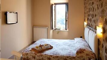A bedroom with a bed, a window, a radiator, a bedside table, and a wall-mounted shelf.