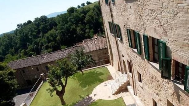 A courtyard with a stone building featuring green shutters, surrounded by a lush green landscape and trees. - Arnolfo B&B (Colle di Val d'Elsa)