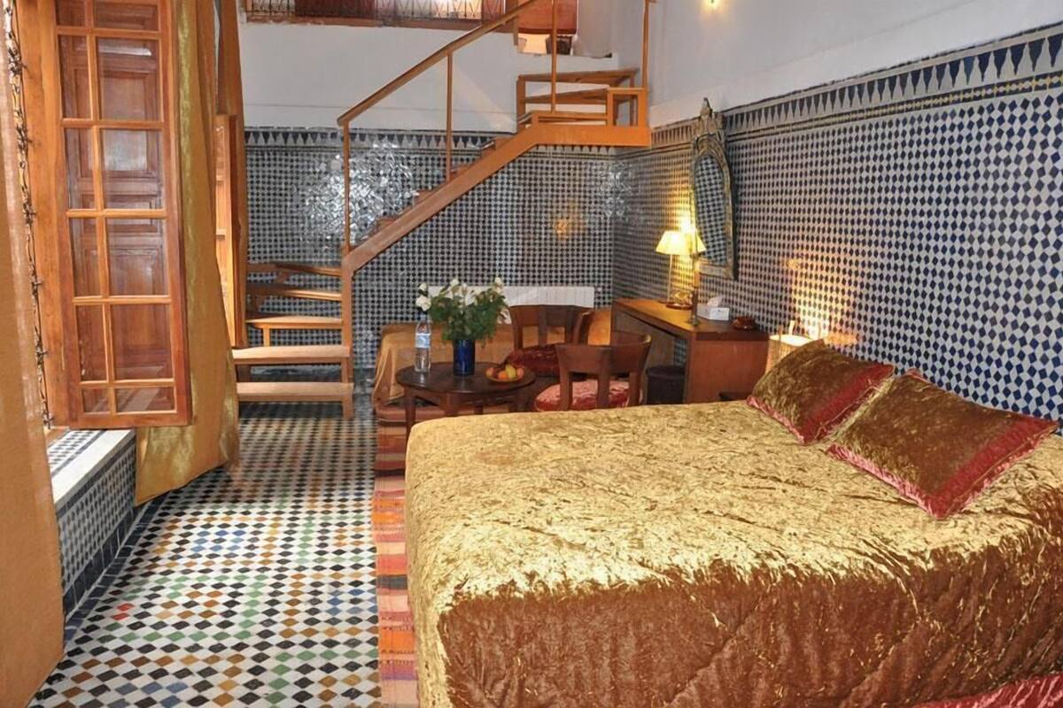 A bedroom with a large bed, a wooden staircase, a desk, and a chair.