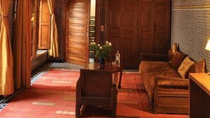 A traditional interior with a wooden sofa, a small table with a vase, and a patterned carpet. - Riad au 20 Jasmins (Fes)
