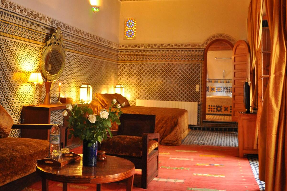 A traditional Moroccan interior with a patterned ceiling, a chandelier, a sofa, a coffee table, and a decorative mirror.