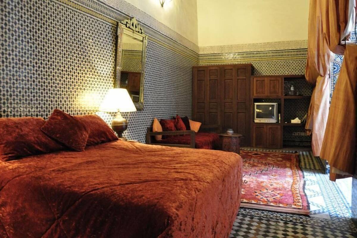 A room with a large bed, a small table, a chair, a television, and a cabinet.