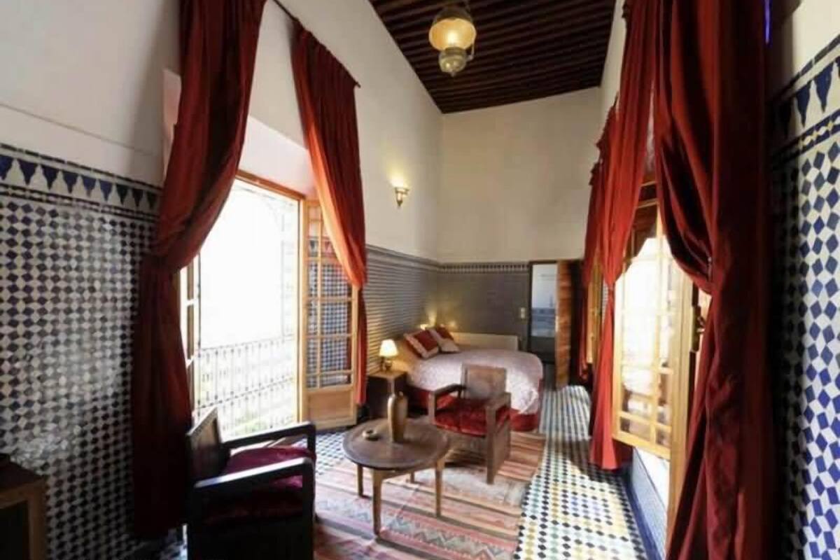 A room with a bed, a chair, a small table, and a window with curtains.