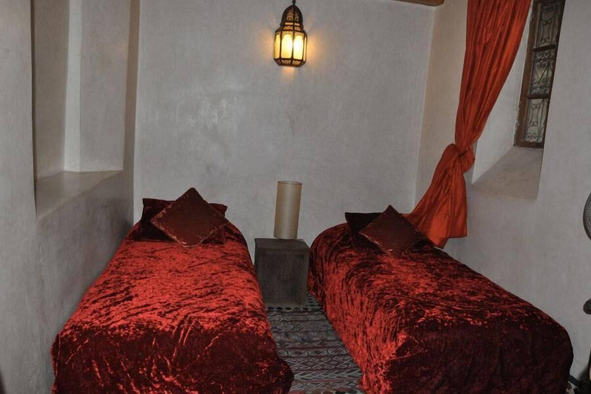 A room with two beds, a wall-mounted light fixture, and a window with a curtain.