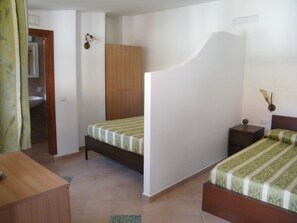 A bedroom with a bed, a nightstand, a wooden wardrobe, and a bathroom visible through an open door. - Hotel Villaggio Tabù (Centola)