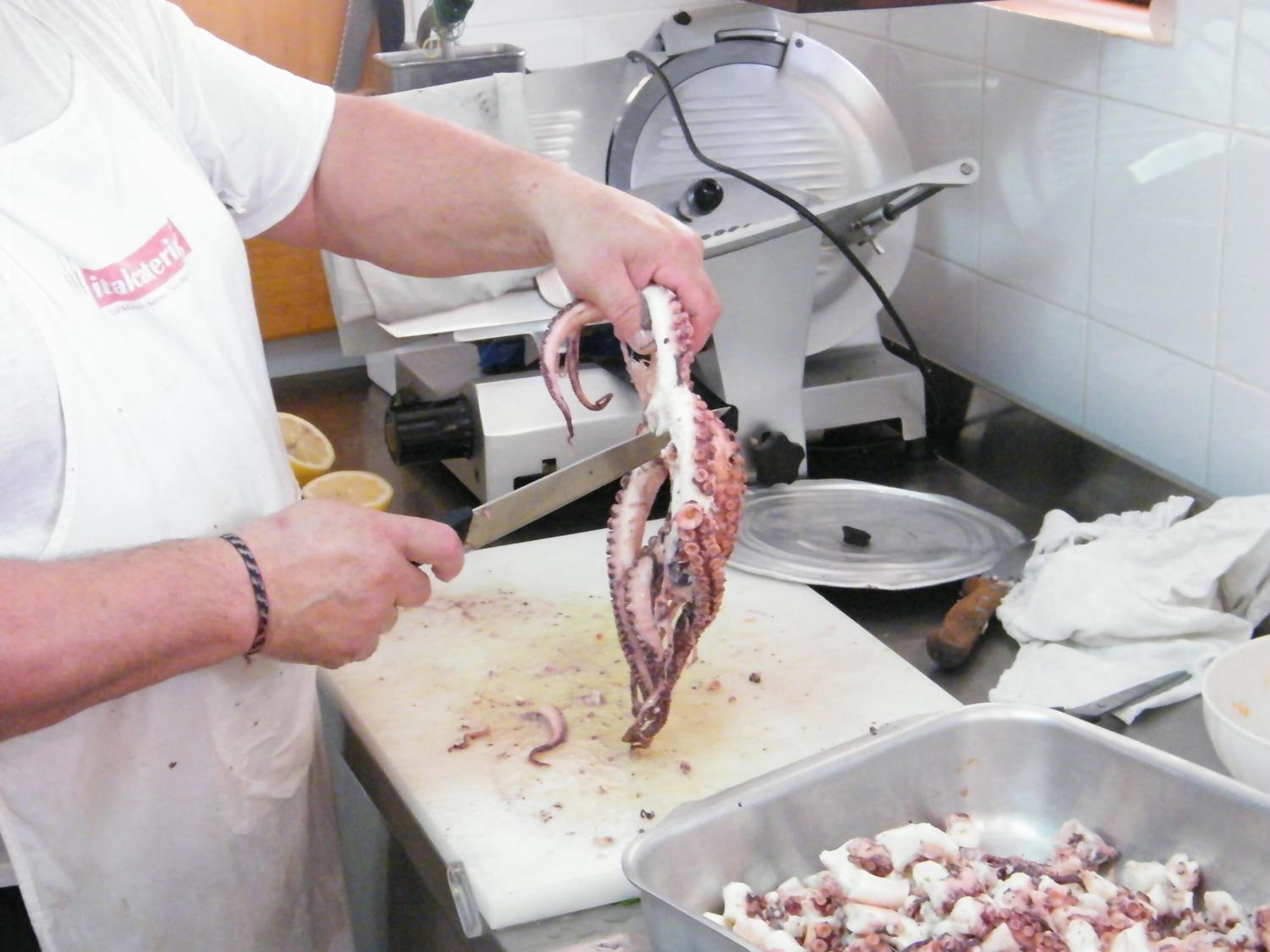 A person preparing food, specifically cutting an octopus on a cutting board in a kitchen.