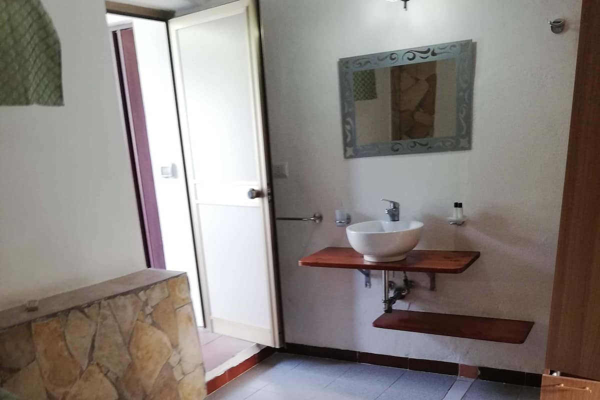 A hotel room with a bed, a bathroom with a sink and mirror, and a stone accent wall.