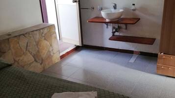Une chambre d’hôtel avec un lit, une salle de bain dotée d’un lavabo et d’un miroir, et un mur décoratif en pierre.