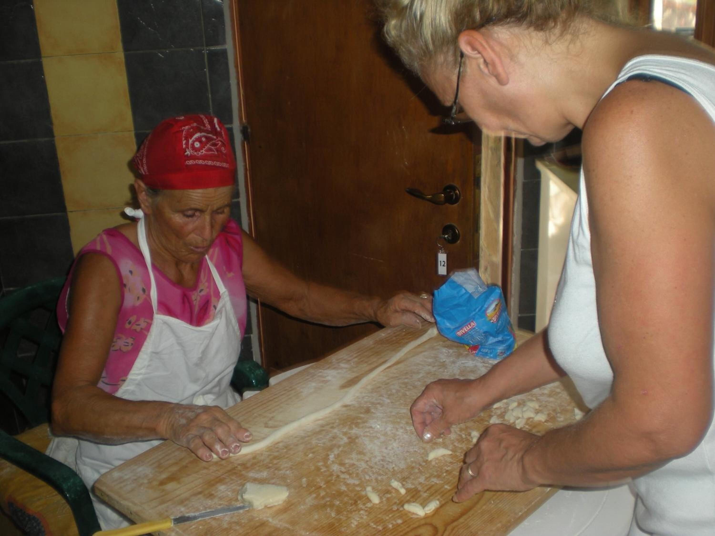 Two people preparing food on a wooden table with a rolling pin and a bag of flour.