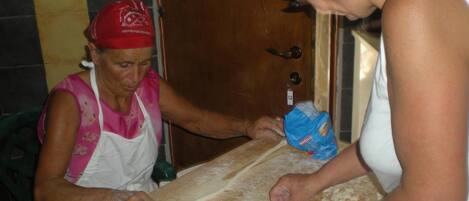 Two people preparing food on a wooden table with a rolling pin and a bag of flour.