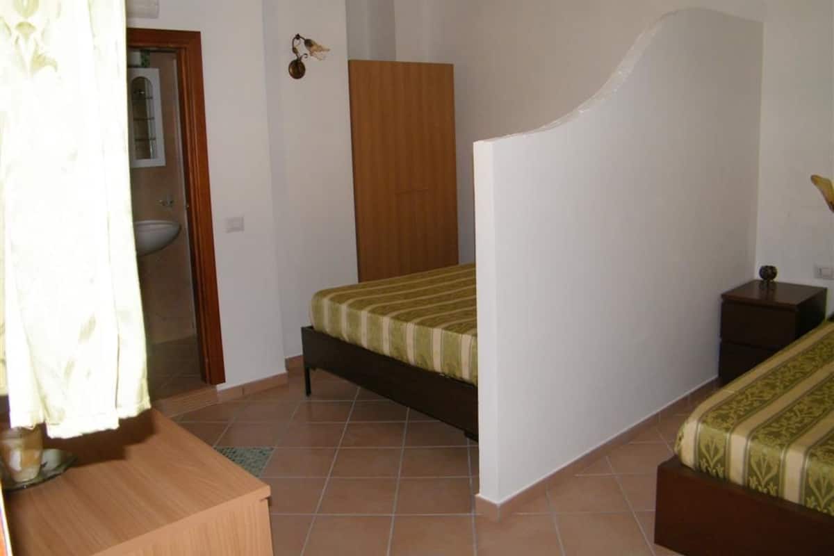 A bedroom with a bed, a wooden nightstand, a small table, and a bathroom visible through an open door.