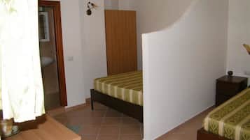 A bedroom with a bed, a wooden nightstand, a small table, and a bathroom visible through an open door.