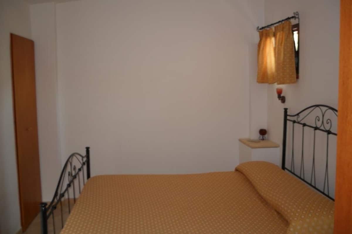 A bedroom with a single bed, a nightstand, a wall-mounted lamp, and a door.