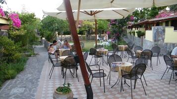 An outdoor patio with tables and chairs, surrounded by greenery and a stone wall.