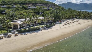 A beachfront resort with multiple bungalow-style buildings, a sandy beach with umbrellas, and a clear view of the ocean. - Hon Tam Resort (Nha Trang)