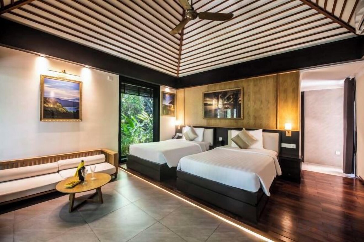 A hotel room with a bed, a sofa, a small table, and a ceiling fan.