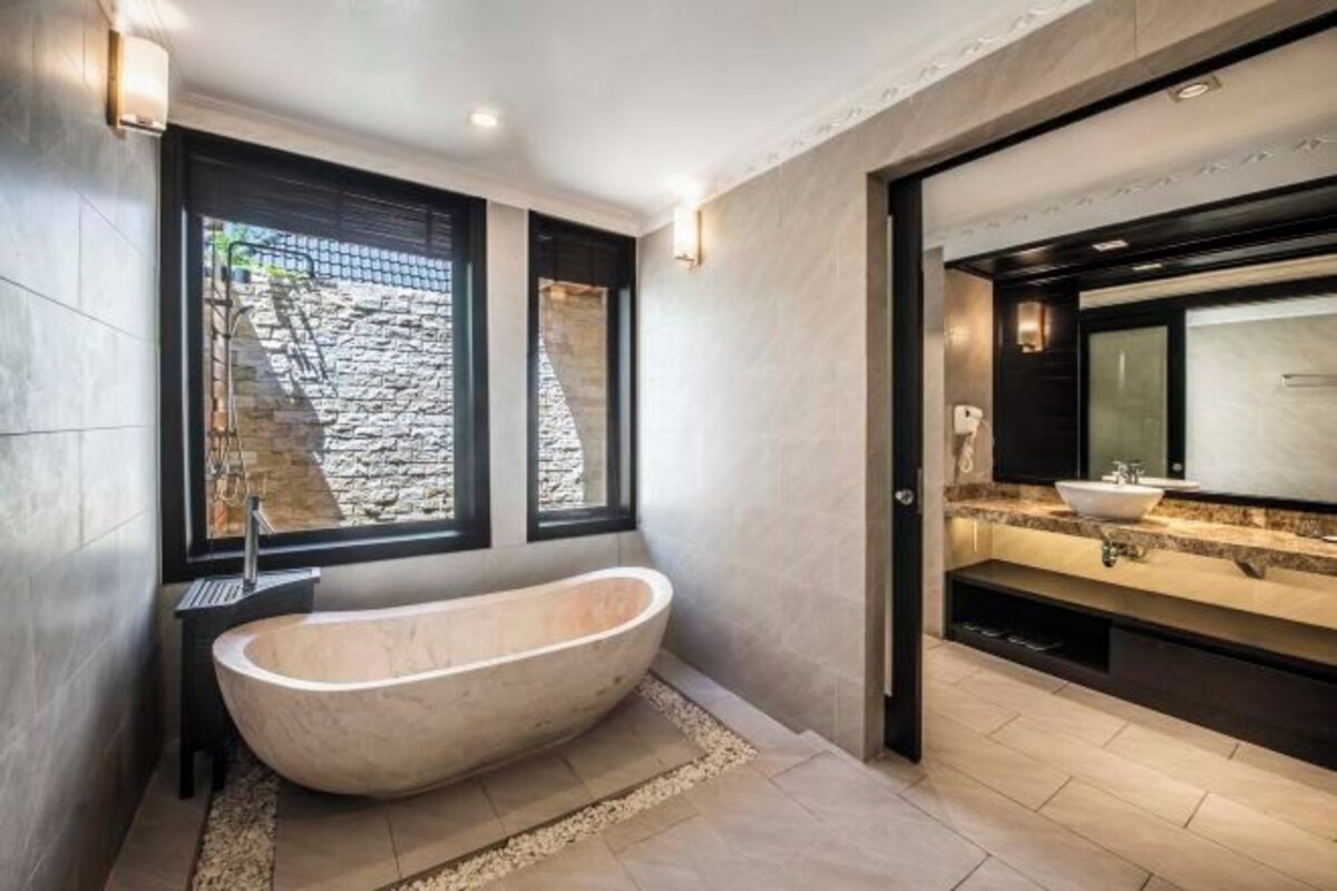 A modern bathroom with a freestanding bathtub, a large mirror, and a stone wall.