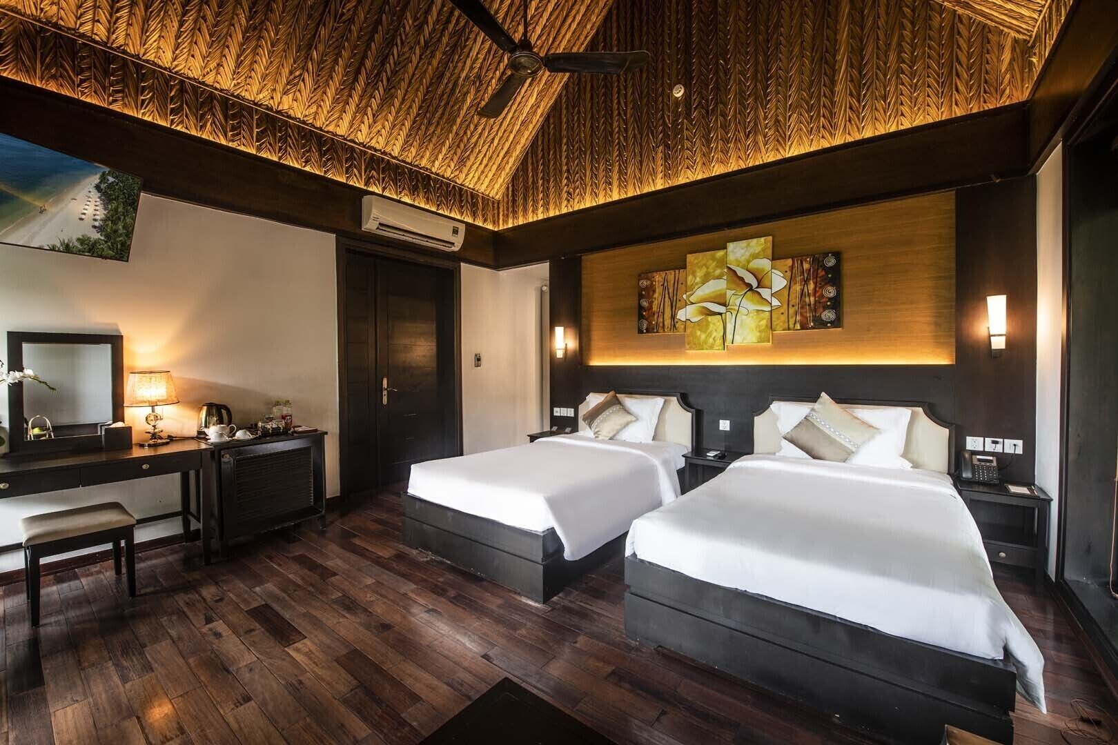 A hotel room with two beds, a desk, a mirror, and a large artwork on the wall.