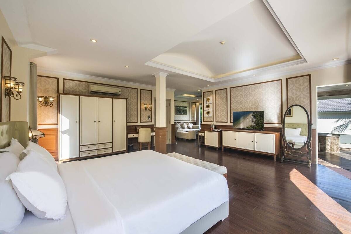 A spacious bedroom with a large bed, a desk, a chair, and a television.