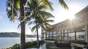 A hotel with a patio overlooking a body of water, palm trees, and a modern building with large windows. - Hon Tam Resort (Nha Trang)