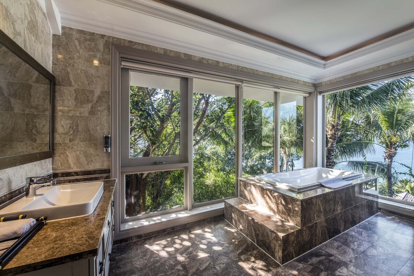 A modern bathroom with a large window, a bathtub, and a sink.