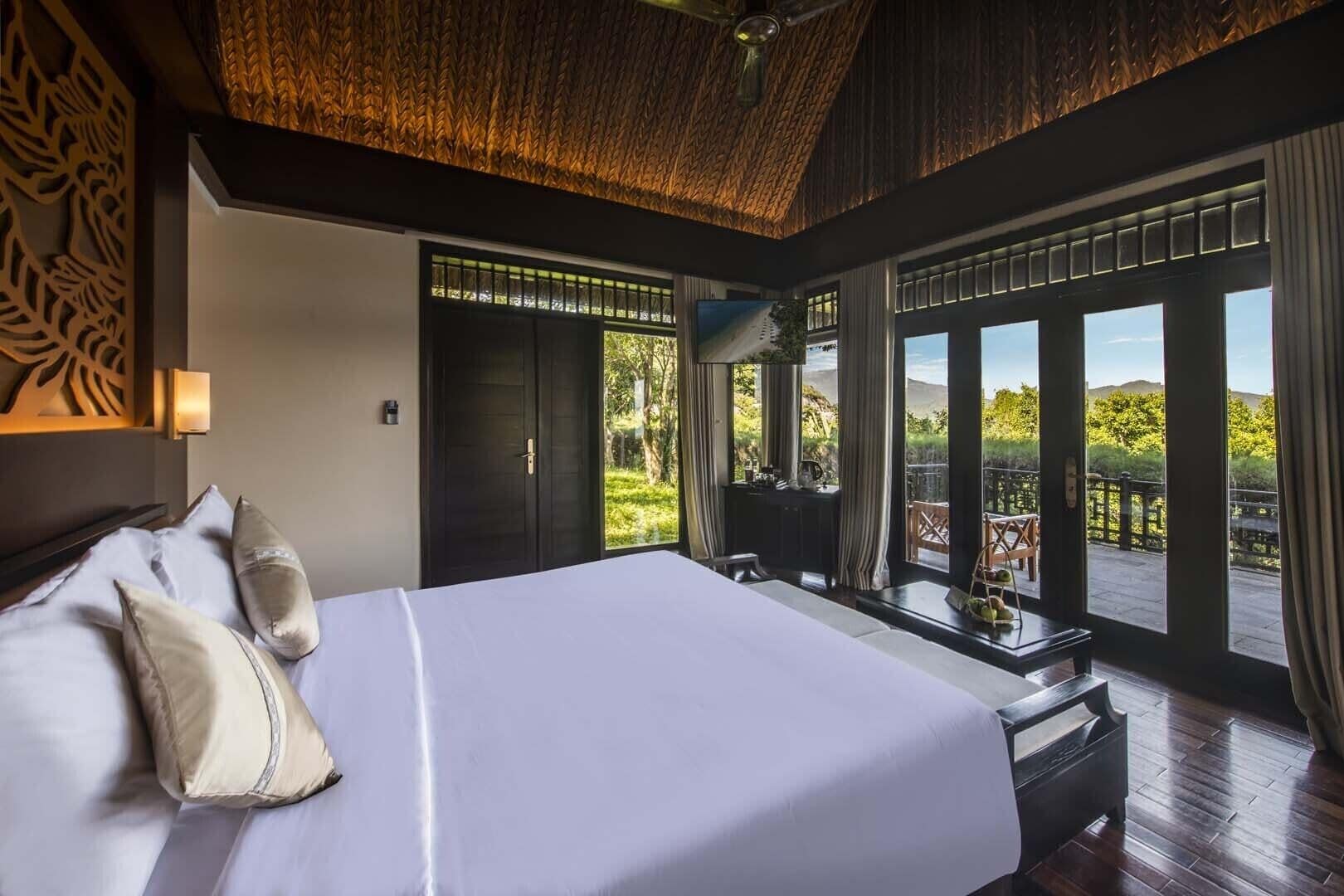 A bedroom with a large bed, a desk, and a view of the outdoors.