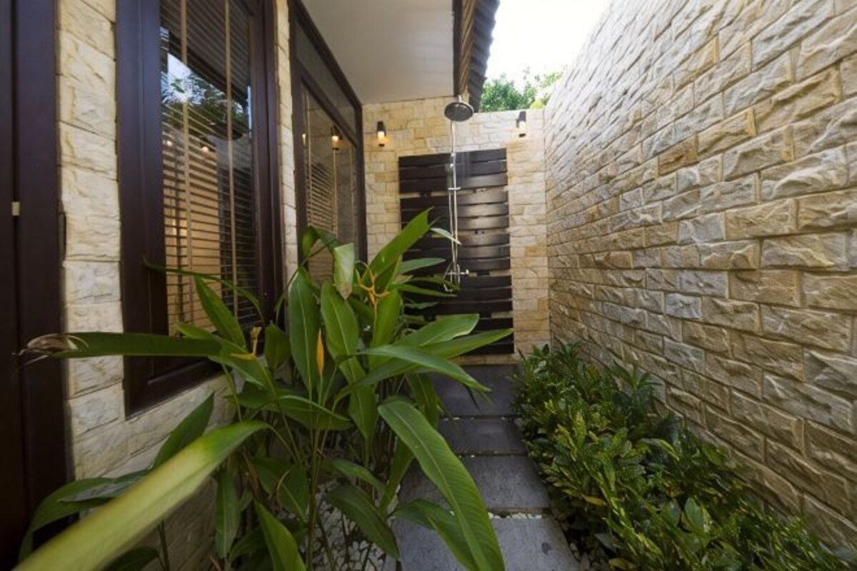 A narrow outdoor corridor with stone walls, a door, and a small garden area with plants.