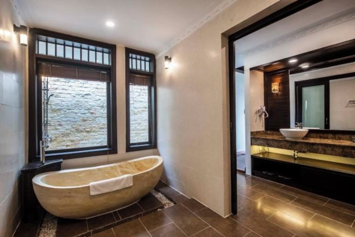 A modern bathroom with a freestanding bathtub, a large mirror, and a stone wall view.