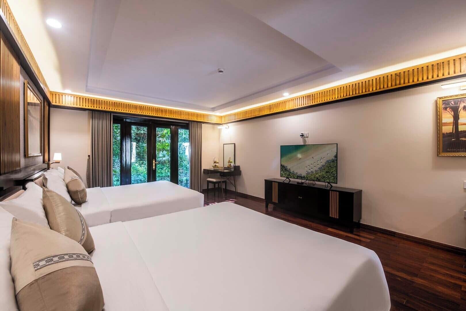 A hotel room with two beds, a TV, a desk, and a large window with a view of greenery.