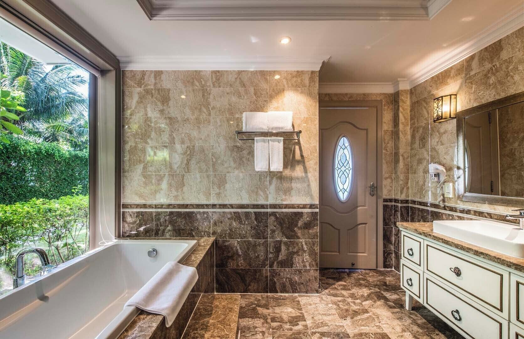 A bathroom with a bathtub, a vanity with a large mirror, and a door with a stained glass window.
