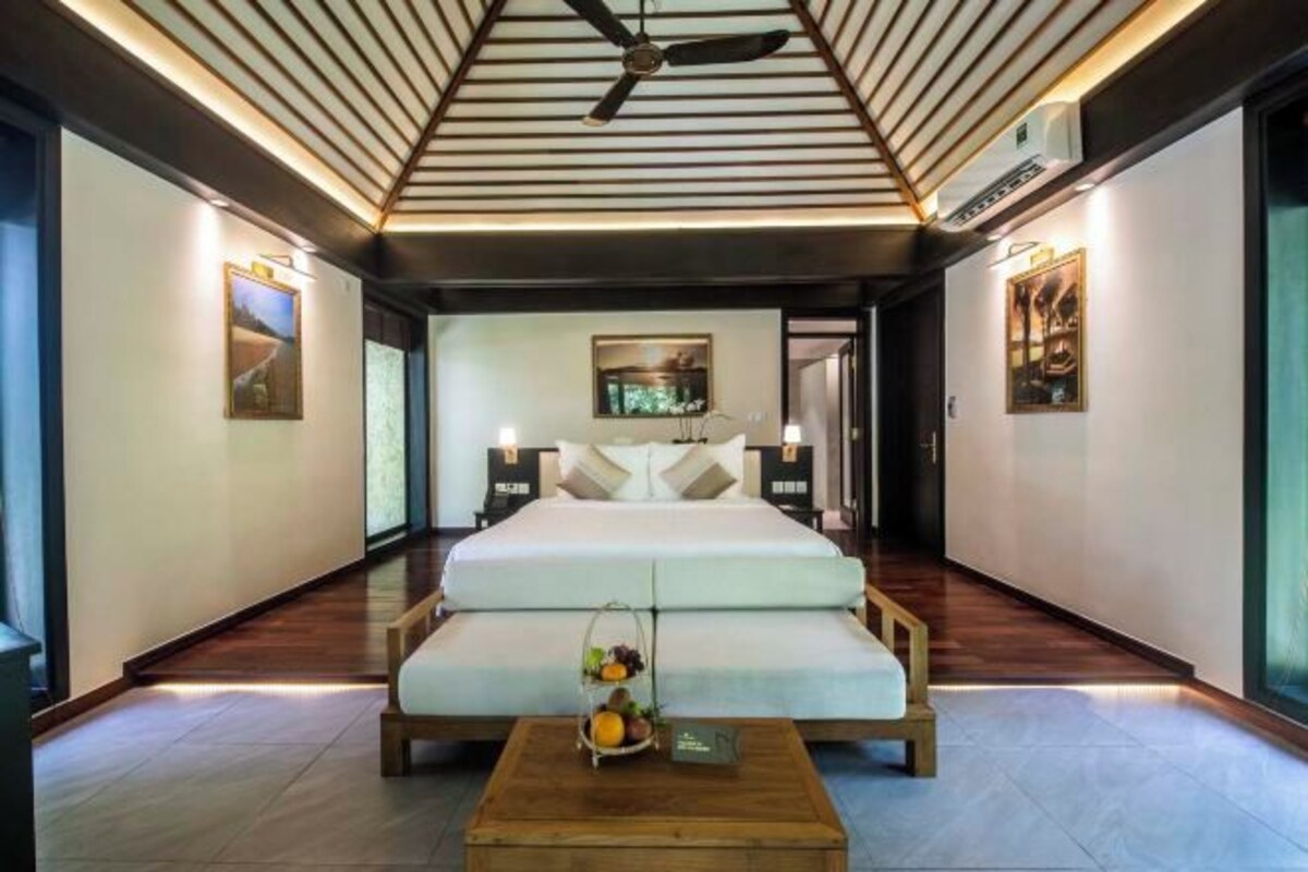 A modern hotel room with a large bed, a wooden coffee table with fruit, and a ceiling fan.