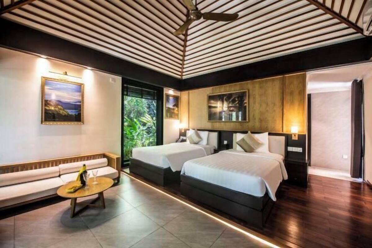 A modern hotel room with two beds, a sofa, a coffee table, and a ceiling fan.