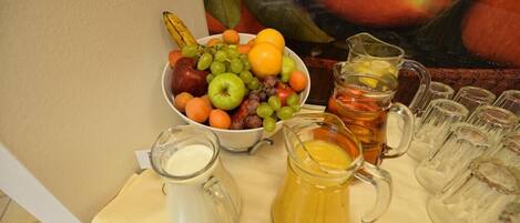 Una mesa con un cuenco de fruta, una jarra de té y una jarra de jugo.