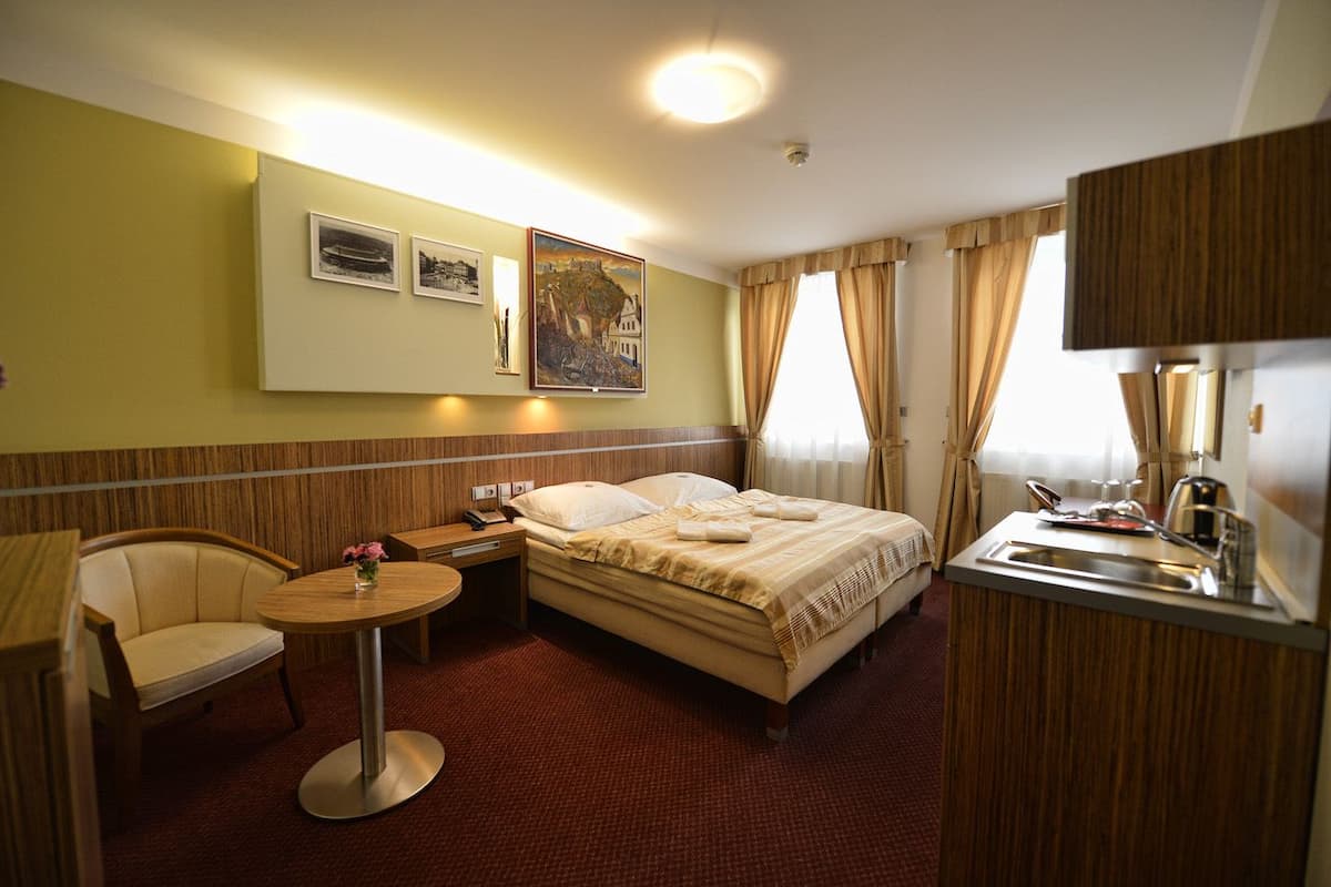 A hotel room with a bed, bedside table, chair, and a small round table with a vase.