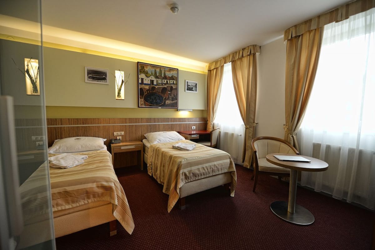 A hotel room with two single beds, a small desk, a chair, and a window with curtains.