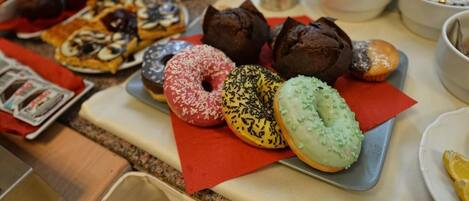 Una mesa de buffet con diversos pasteles y productos de panadería, incluyendo rosquillas y muffins.