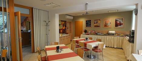 Un comedor con mesas y sillas, una cocina al fondo y un mostrador tipo bufé.