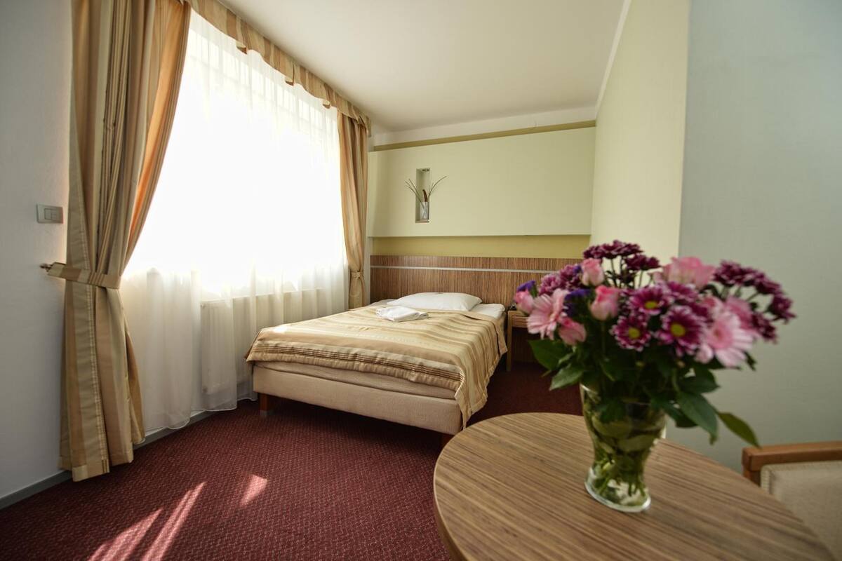 A hotel room with a bed, a bedside table, a vase of flowers, and a window with curtains.