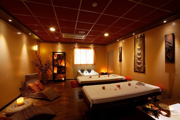 Un cuarto de spa con dos camas, una camilla de masaje, un estante decorativo y una ventana con cortinas.